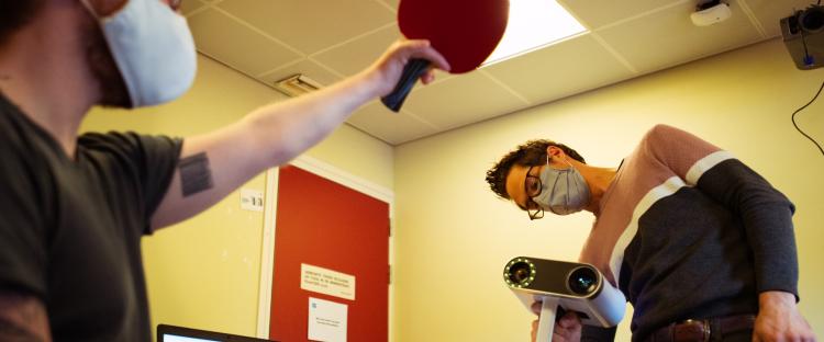 2 personen; één houdt een ping pong palletje, andere een speciale camera