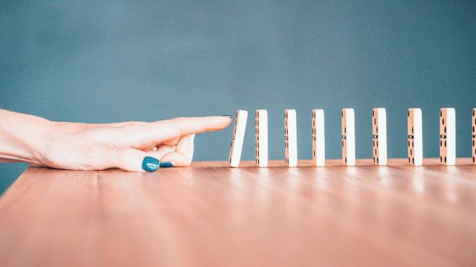 Rij dominosteentjes, met een aankomende vinger die het eerste steentje gaat omduwen