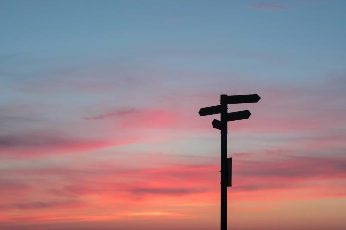 Wegwijzers naar verschillende richtingen, tegen een achtergrond van een kleurrijke zonsondergang